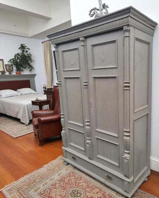 Antique pine wardrobe with two panelled doors and a lower drawer, rustic farmhouse style, grey-painted finish with iron handles.