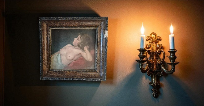 Framed painting of a nude figure on a wall with a candlelit sconce.